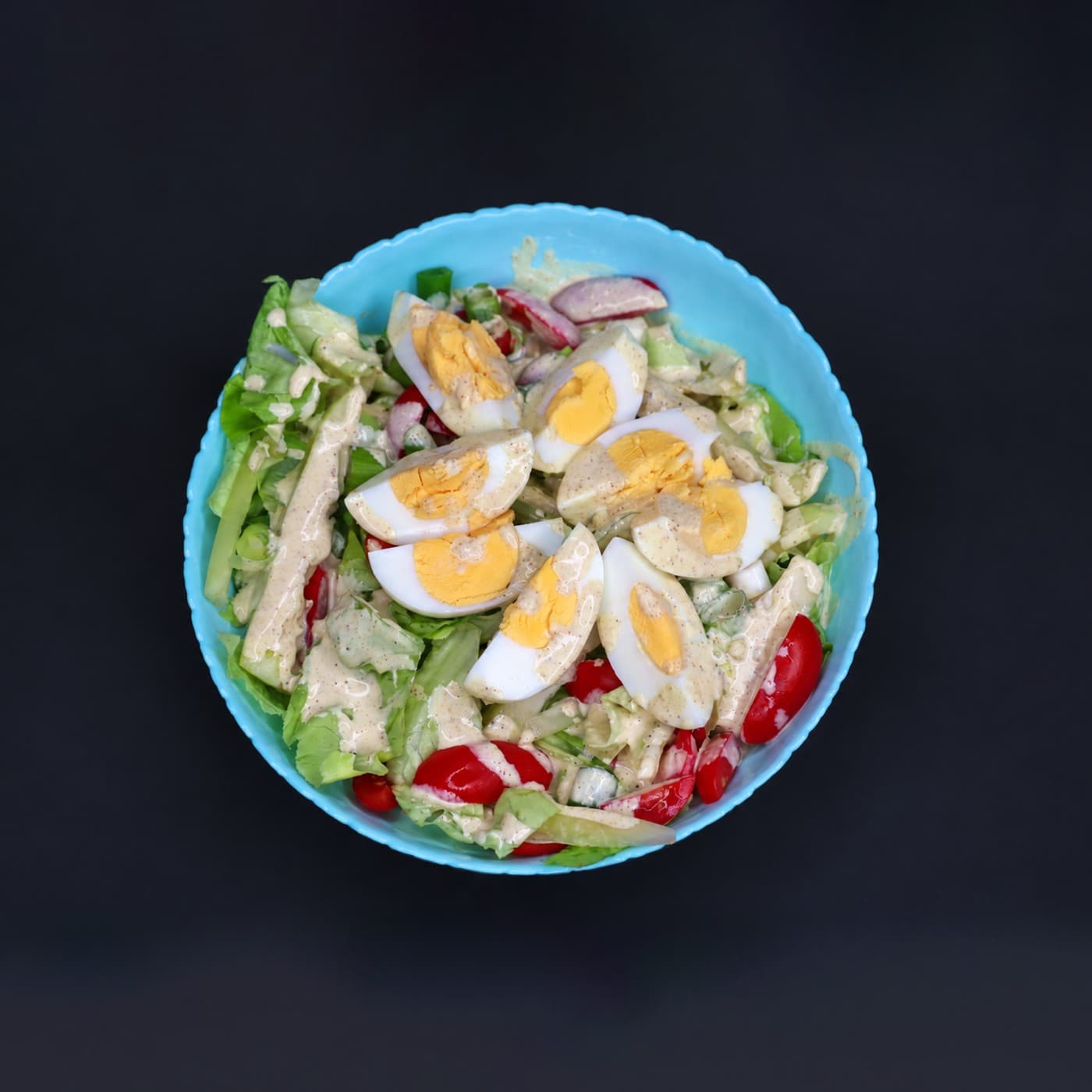 Salata sa jajima, paradajzom, rotkvicom i zelenom salatom u plavoj činiji.